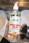 A bottle of eco dish soap citrus held in front of dirty dishes, for an eco-friendly and sustainable home.