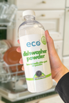 A bottle of eco dishwasher powder unscented held in front of a dishwasher, for an eco-friendly and sustainable  home.
