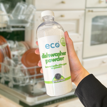 A bottle of eco dishwasher powder unscented held in front of a dishwasher, for an eco-friendly and sustainable  home.